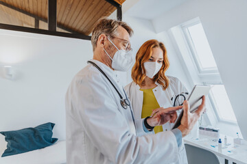Doctor discussing over digital tablet with coworker while standing at clinic