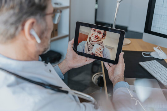 Male healthcare worker talking to patient over digital tablet while sitting at doctor's office