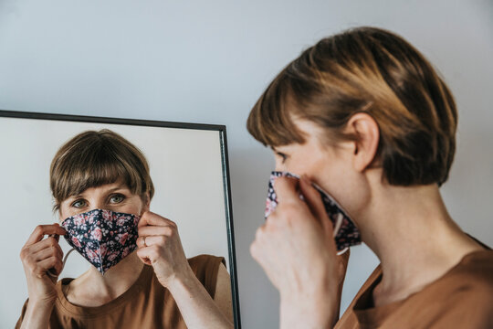 Brown haired woman wearing protective face mask while looking in mirror during pandemic