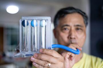 Old man uses a Tri-ball Incentive Spirometer for check his lung function.