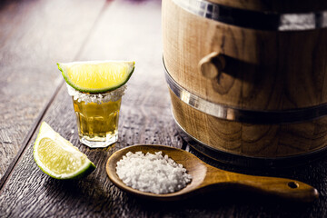 glass of tequila, distilled drink with salt and lemon, with oak barrel next to it