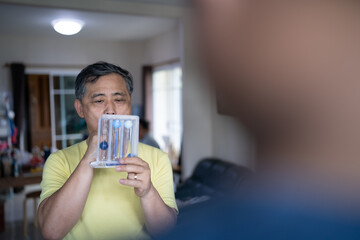 Old man uses a Tri-ball Incentive Spirometer for check his lung function.