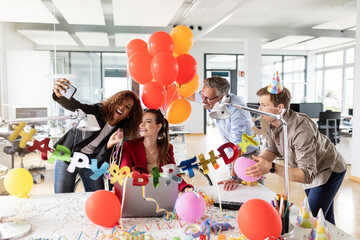 Cheerful businesswoman taking selfie with colleagues while during birthday celebration in office