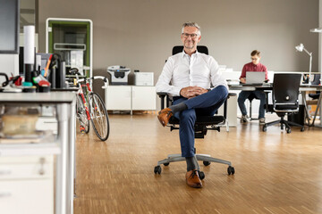 Smiling businessman with legs crossed at knee sitting on chair in office