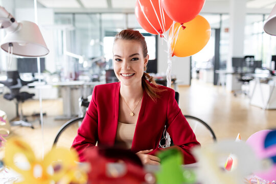 Smiling young businesswoman sitting in office during birthday celebration