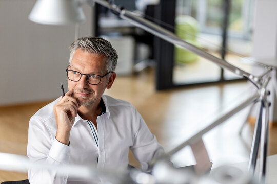 Smiling businessman with hand on chin looking away while sitting in office