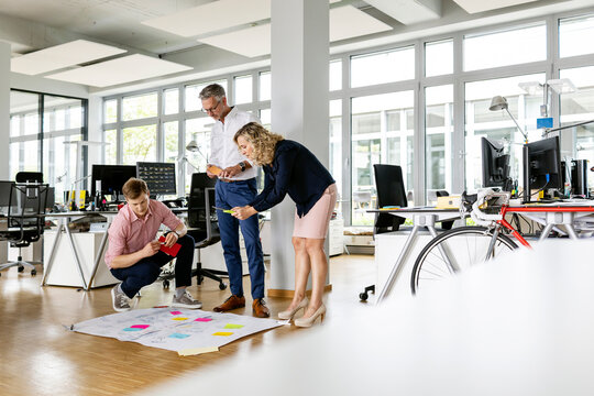 Businesswoman by colleagues photographing business plan in open plan office