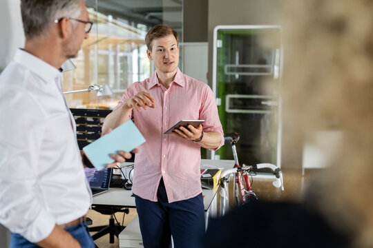 Young businessman with digital tablet explaining plans to colleagues in office