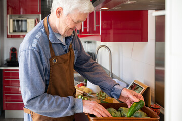 Senior man arranging vegetables while standing in kitchen at home