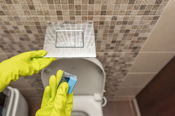 Toilet cubes cleaner in hand. A hand lowers a disinfectant cube into the water of a toilet bowl built into the wall.