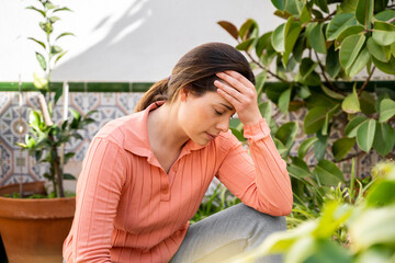 Tensed young woman with head in hand sitting in garden