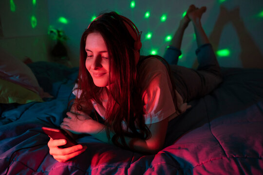 Young woman using mobile phone while lying on front in bedroom