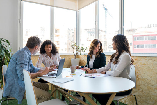 Male and female colleagues discussing while sitting at desk in office