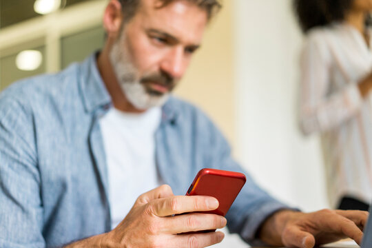 Male entrepreneur with office colleague using smart phone while working in office