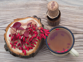 Berries and leaves of the useful berberis plant and a tea in a mug, berberis cider, syrup in a bottle on a wooden background, top view. Seasonal red barberry fruit and drinks for use  food