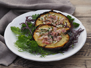 Fried potatoes in the skin with bacon, herbs in a white plate with a napkin on a wooden table, closeup. Delicious healthy dish with vegetables, cooked on the grill