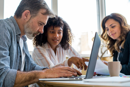 Male and female colleagues discussing over laptop while sitting in office