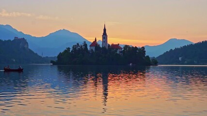 Slovenia, Lake Bled. Sunrise over the Church of the Mother of God. Europe, Alps. Fishermen crossing the lake in a boat just before sunrise.