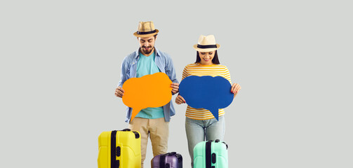 Two people with orange and blue dialog speech balloons standing isolated on studio background. Man and woman with travel suitcases showing tourist news announcement informing placard message bubbles