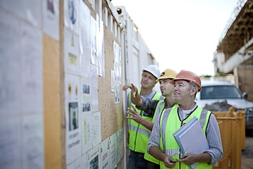 Three male construction workers inspecting bulletin board at construction site
