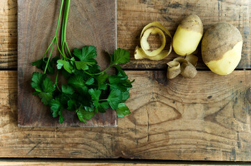 Half peeled potatoes and parsley leaves on rustic wooden background