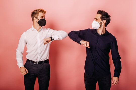 Male entrepreneurs wearing protective face mask greeting with elbow bumps while standing against colored background