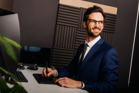 Smiling businessman looking away while using graphics tablet at desk in office
