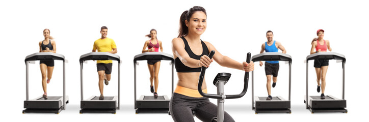 Young woman riding a stationary bike and other people running on treadmills