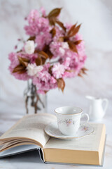 Cup of coffee,open book  and flowering  cherry tree branches on white marble background.Spring concept.Romantic still life.