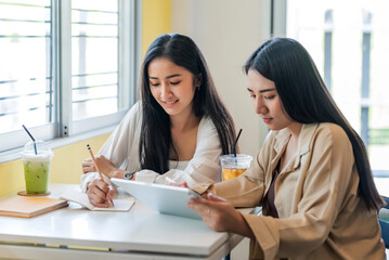 Two young woman are learning collaboration using taking notes and tablet at the café.