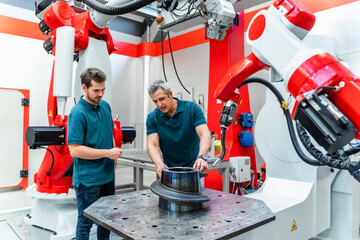 Mature engineer explaining welding machinery to colleague in factory