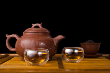 Tea ceremony. Wet clay teapot with red tea Lapsang souchong and glass thermo cups on a black background. Copy space.