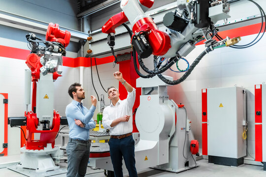 Mature entrepreneur discussing over robotic welding torch with colleague in factory