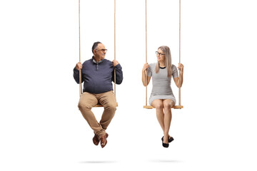 Mature man and a young woman sitting on swings and looking at each other