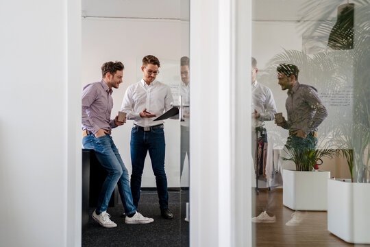 Male entrepreneurs discussing over clipboard seen through doorway at office
