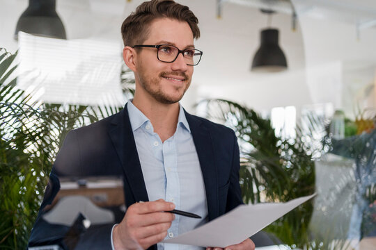 Smiling male entrepreneur with document seen through glass at office