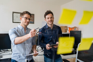 Smiling male colleagues discussing over adhesive notes at office