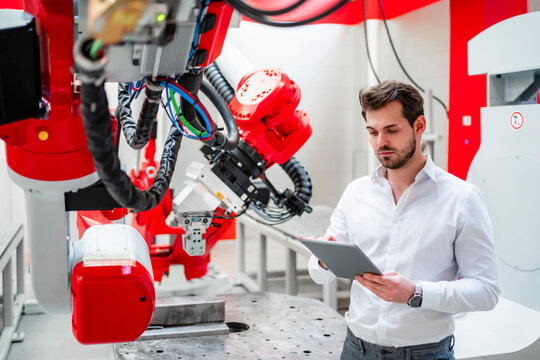 Young man using digital tablet by robotics in factory