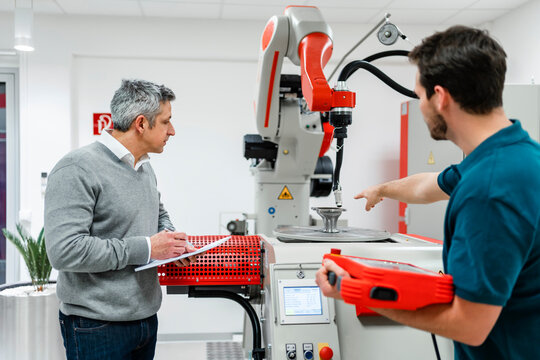 Engineer pointing at machinery while discussing with colleague in industry