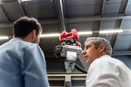 Male engineers discussing at robotic arm in factory