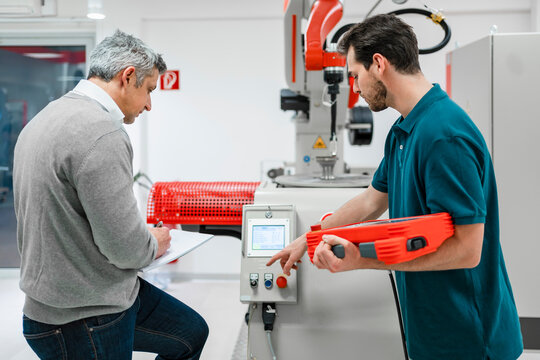 Young male engineer holding control while operating machine by mature entrepreneur in industry