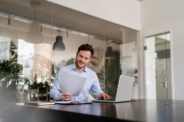 Businessman with document working on laptop at office