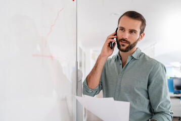 Businessman talking on mobile phone while standing by whiteboard at office