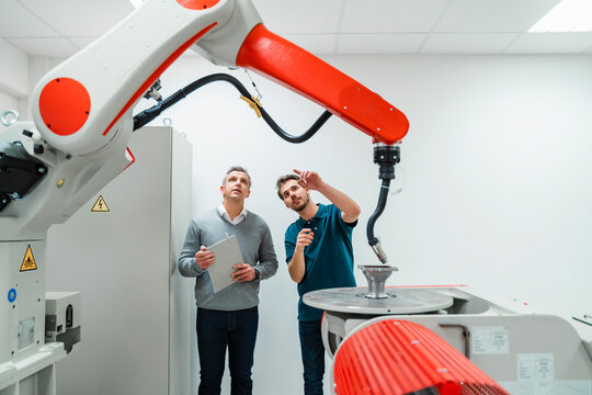 Young male engineer pointing at machinery while discussing with mature entrepreneur in factory