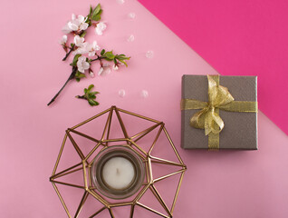 Layout on a pink background. a candle, a packed gift box, a tree branch blooming with flowers. spring Flat lay