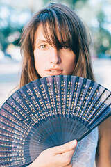 Vertical portrait of a beautiful brunette young woman with blue hand fan.