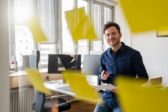 Smiling businessman with document looking at adhesive notes at office