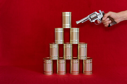 Human hand holding gun against stack of tin cans