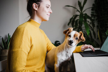 Young woman working on digital tablet while sitting with pet at home office