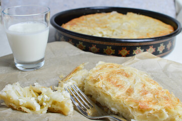 Traditional Balkan, Serbian cheese pie, burek, borek on the paper, with glass of yogurt in the background, closeup